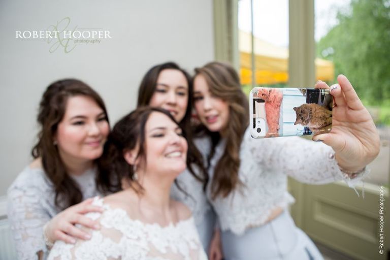 Bride and bridesmaids taking a selfie with their iPhone on wedding day at Hampton Court House Surrey