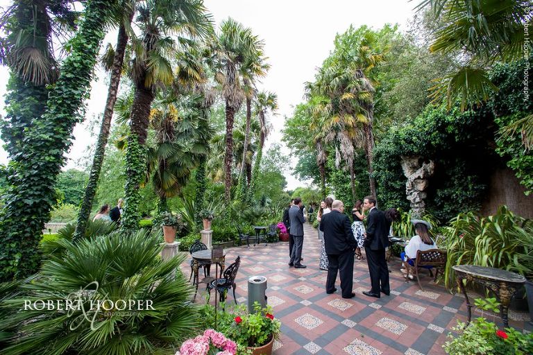 Wedding guests mingling in tropical garden outside Hampton Court House Surrey