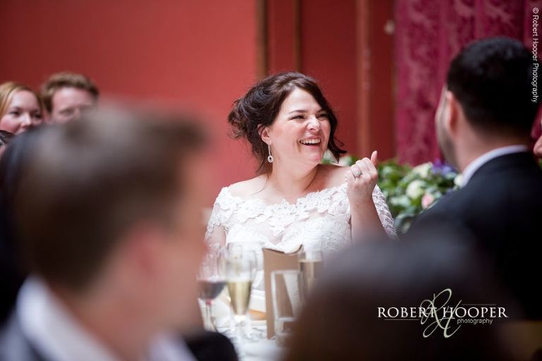 Bride laughing at husband's speech at wedding breakfast at Hampton Court House Surrey