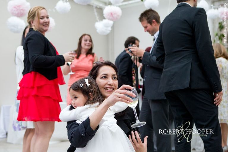 Wedding guest cuddles flower girl on dance floor at evening reception at Hampton Court House Surrey