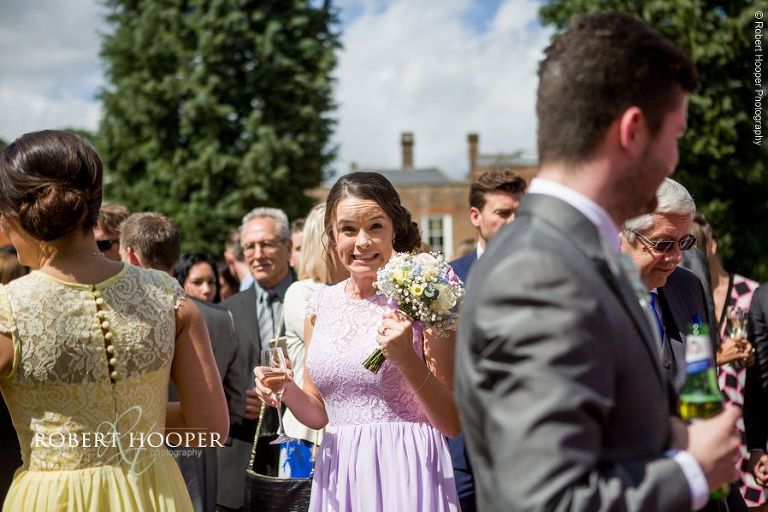 Bridesmaid pulling funny face during champagne reception for wedding day in gardens at Wotton House Surrey