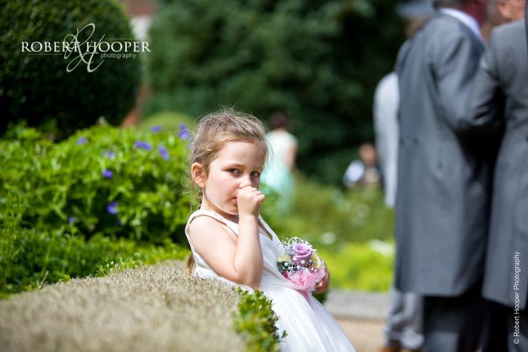 Cute flower girl sucking her thumb during champagne reception on wedding day at Wotton House Dorking Surrey