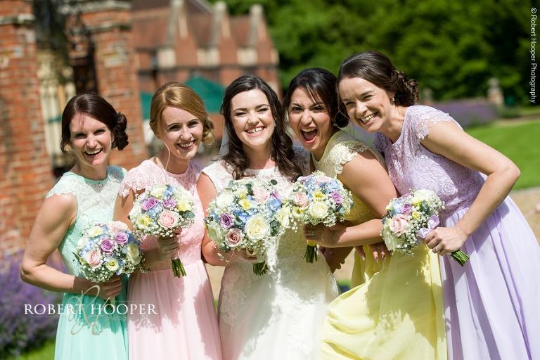 Bridesmaids in pastel colour dresses laughing together on wedding day at Wotton House wedding Surrey