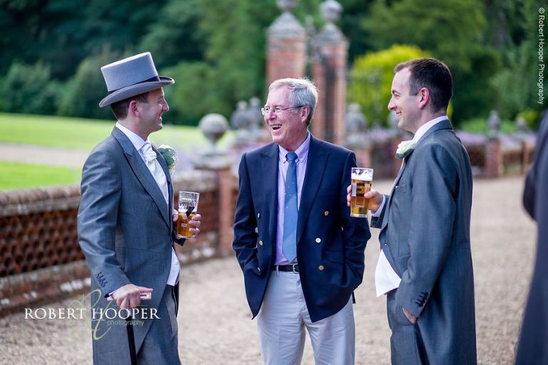 Wedding guests and groom in top hat and tails chatting in gardens at Wotton House Dorking Surrey