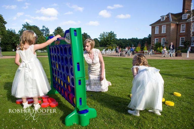 Bride plays Connect 4 with flower girls on lawn on wedding day at Chilston Park Maidstone Kent