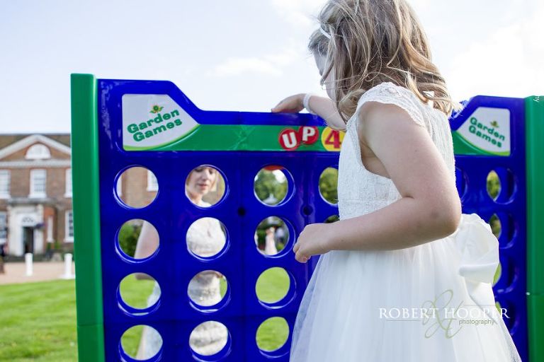 Bride plays Connect 4 with flower girls on lawn on wedding day at Chilston Park Maidstone Kent