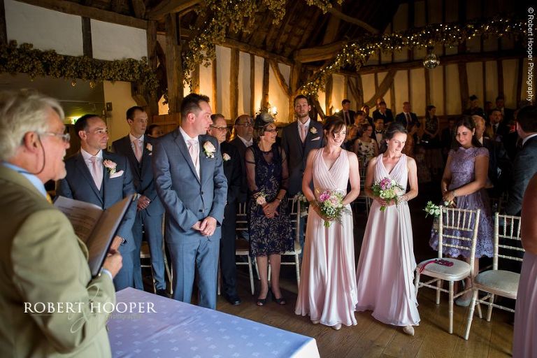 Bridesmaids walk down the isle at wedding ceremony held in the barn at The Crown Inn Pishill Oxfordshire