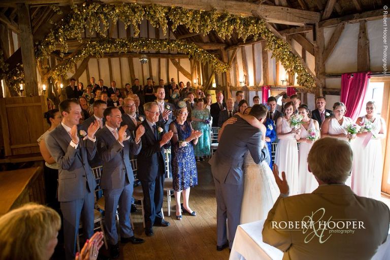 Bride and groom kiss and cuddle during civil wedding ceremony in the barn at The Crown Inn Pishill Oxfordshire