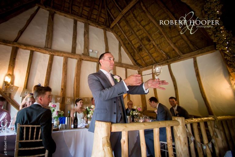 Best man taps his glass to get wedding guests attention for speeches during wedding breakfast at The Crown Inn Pishill Oxfordshire