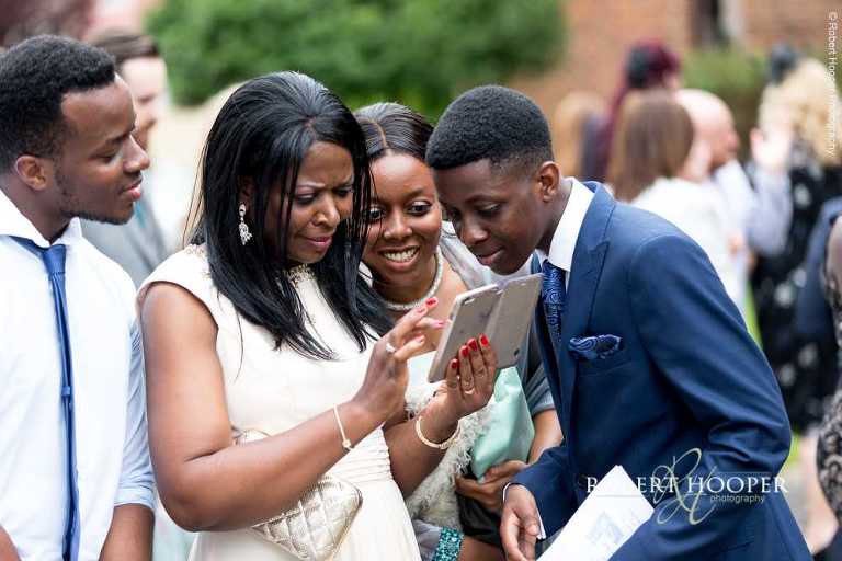 Wedding guests looking at photo taken on their iphone at wedding at St John the Divine Church South Croydon Surrey